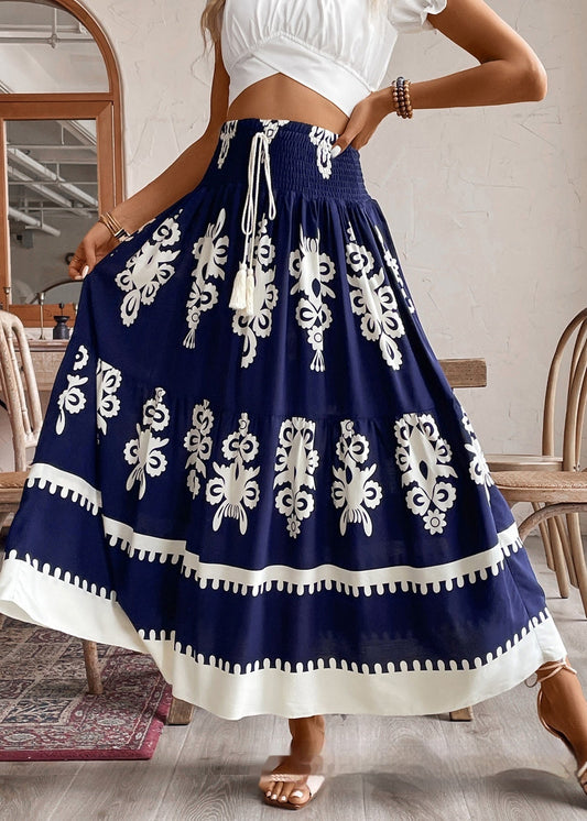 Frau in weißem Crop-Top und blau-weißem Boho-Rock mit Blumenmuster, steht in modernem Café. Sommermode, Boho-Stil, Damenbekleidung.