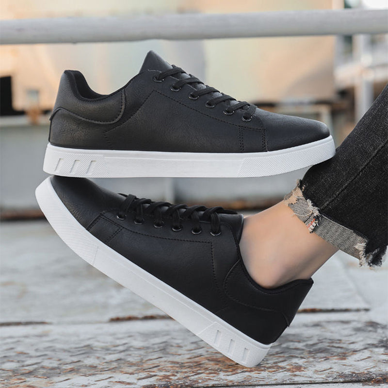 Schwarze Sneaker mit weißer Sohle, getragen von Person in Jeans. Modische, bequeme Freizeitschuhe für Damen und Herren. Ideal für Alltag und Sport.