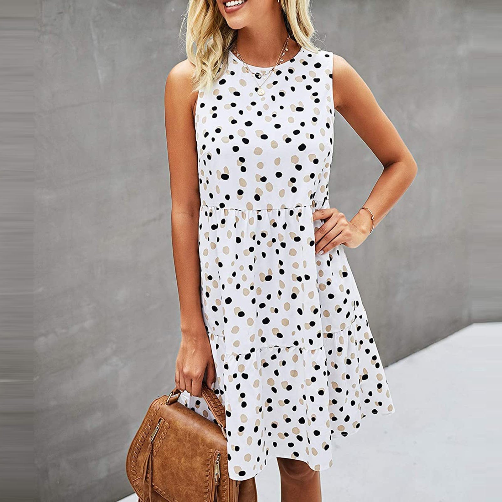 Frau in ärmellosem, weißem Kleid mit schwarzen Punkten, hält braune Handtasche. Sommermode, elegantes Design, trendiges Outfit.