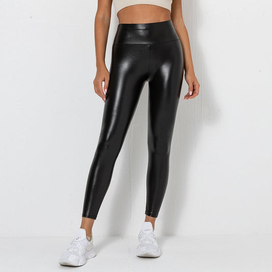 Frau trägt schwarze, glänzende Lederleggings und weiße Turnschuhe vor weißem Hintergrund. Modetrend, Damenbekleidung, sportlich-eleganter Look.
