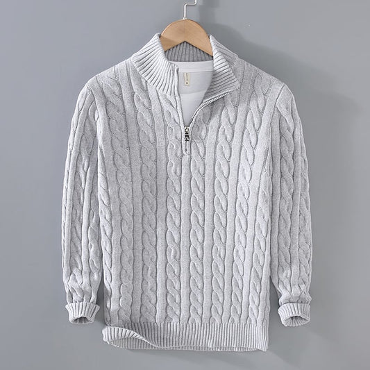 Grauer Strickpullover mit Zopfmuster und Reißverschluss, hängend an einem Holzkleiderbügel vor grauem Hintergrund. Wintermode, Herrenbekleidung.