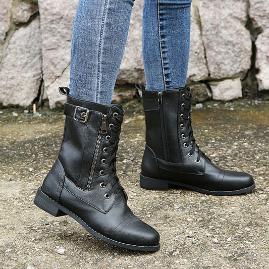 Schwarze Lederstiefel mit Schnürung und Reißverschluss, getragen zu blauen Jeans auf steinigem Untergrund. Modische Damenstiefel, Herbstmode.