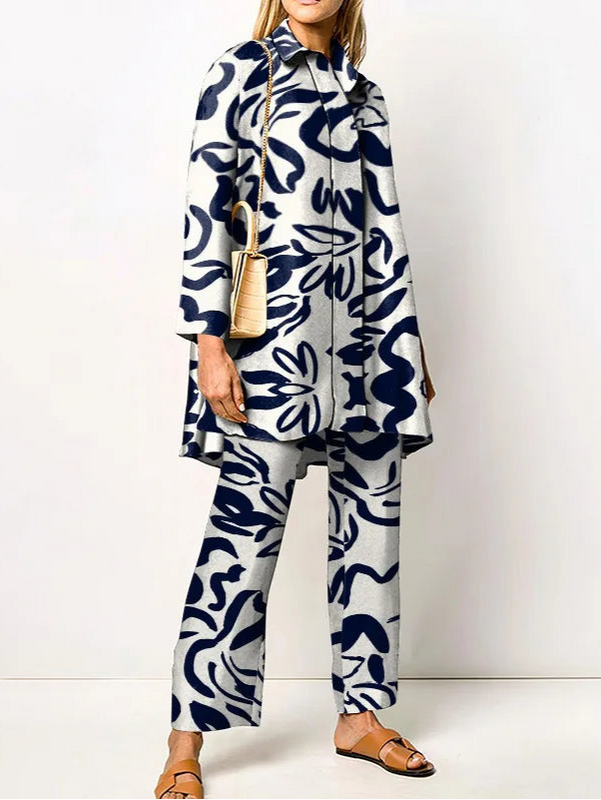 Frau in modernem, blau-weiß gemustertem Anzug mit Mantel, trägt beige Handtasche und Sandalen. Elegante Damenmode, stilvolles Outfit.