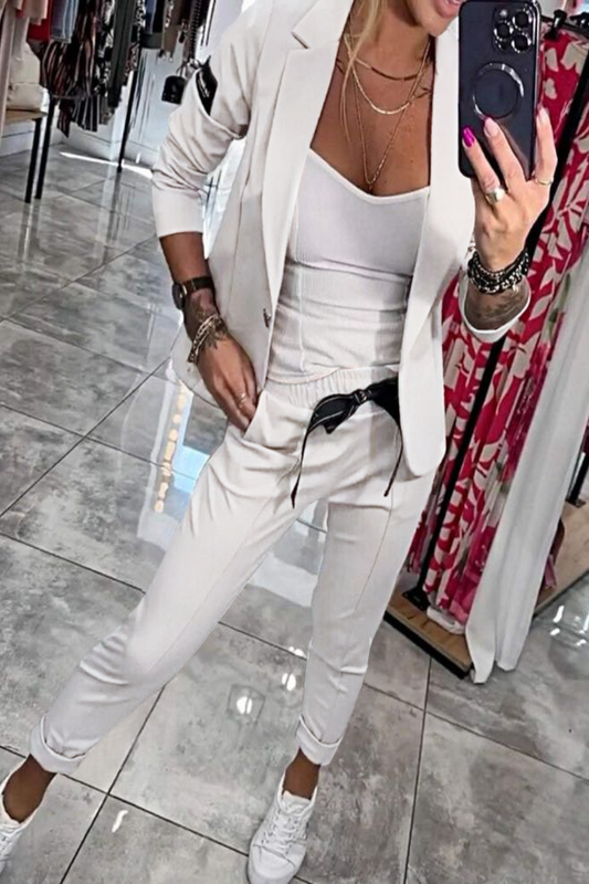 Frau in weißem Anzug mit Smartphone, modisches Outfit, Spiegel-Selfie, elegante Kleidung, moderne Damenmode, stilvolle Accessoires, Boutique-Hintergrund.