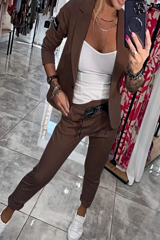 Frau im braunen Anzug mit weißem Top und Sneakers macht Selfie in Boutique. Modetrends, Damenmode, eleganter Freizeitlook.