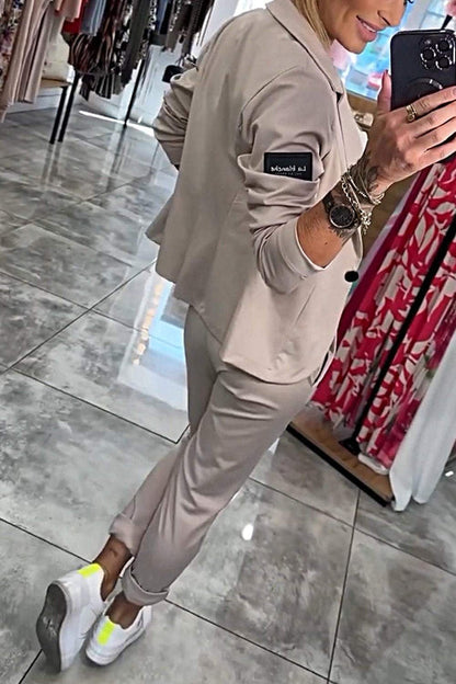Dame in beige Jogginganzug macht Selfie im Spiegel. Modische Freizeitkleidung, weiße Sneaker, Armbänder. Modeboutique im Hintergrund.