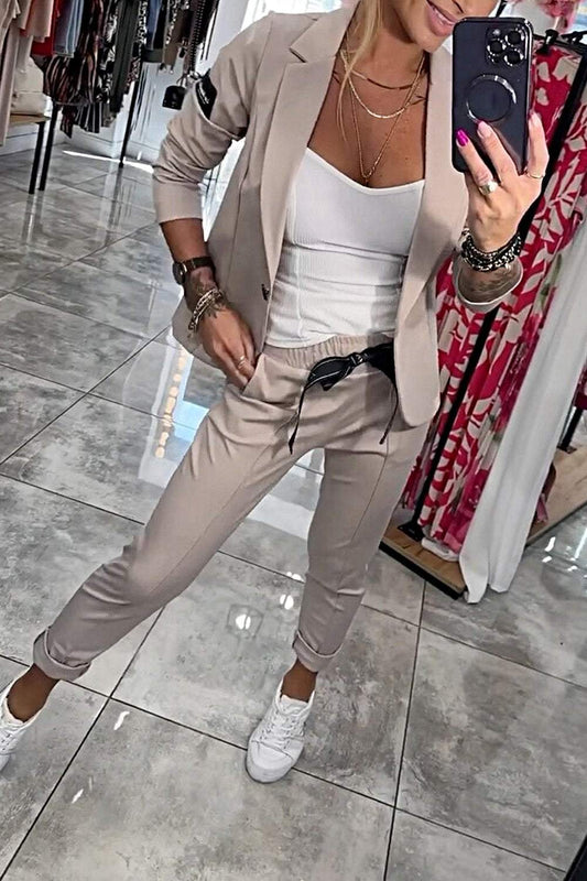 Frau im beigen Anzug mit weißem Top und Sneakers macht Selfie im Spiegel. Modetrends, Business-Casual-Look, stilvolle Damenmode.