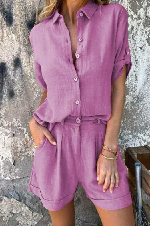 Frau in lila Leinen-Shorts-Set vor rustikaler Wand, Sommermode, lässiger Stil, kurze Ärmel, Knopfleiste, Taschen, trendige Damenbekleidung.
