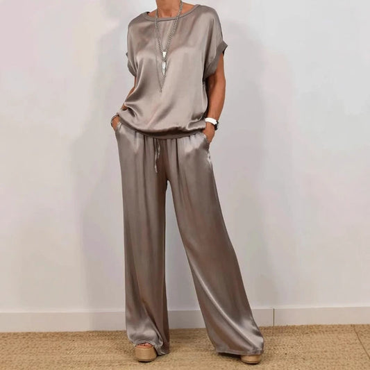 Frau in eleganter, silberner Satin-Hose und passendem Oberteil, trägt lange Halskette und Plateau-Sandalen. Modetrend, stilvolle Damenbekleidung.