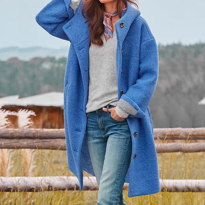 Frau in blauem Wollmantel, grauem Pullover und Jeans vor ländlicher Kulisse. Herbstmode, stilvoller Look, Outdoor-Bekleidung.