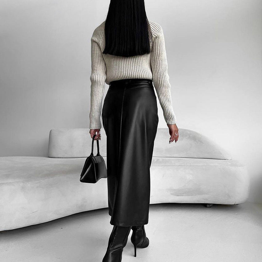 Frau in schwarzem Lederrock und Stiefeln, cremefarbenem Pullover, hält schwarze Handtasche, steht vor modernem, weißem Sofa. Minimalistischer Stil.