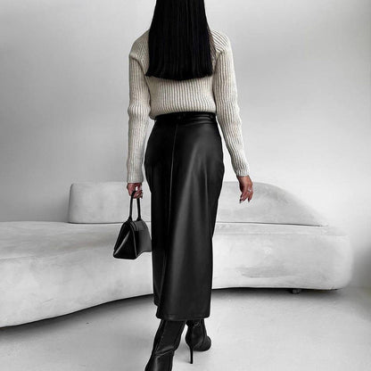 Frau in schwarzem Lederrock und Stiefeln, cremefarbenem Pullover, hält schwarze Handtasche, steht vor modernem, weißem Sofa. Minimalistischer Stil.