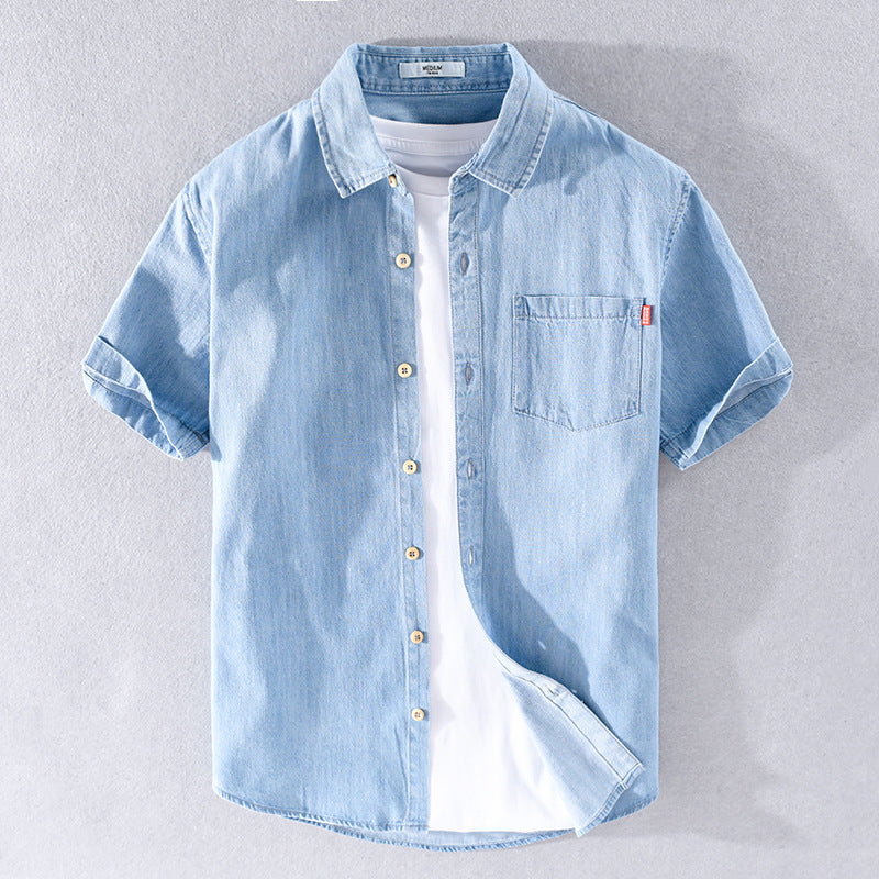 Hellblaues Jeanshemd mit kurzen Ärmeln, Knopfleiste und Brusttasche, über weißem T-Shirt. Modische Herrenbekleidung, lässiger Sommerstil.
