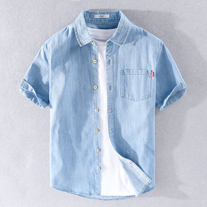 Hellblaues Jeanshemd mit kurzen Ärmeln, Knopfleiste und Brusttasche, über weißem T-Shirt. Modische Herrenbekleidung, lässiger Sommerstil.