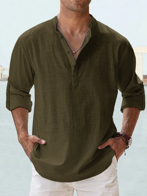 Mann trägt olivgrünes Leinenhemd mit Stehkragen und hochgekrempelten Ärmeln, kombiniert mit weißer Hose. Sommermode, Herrenbekleidung, Freizeitlook.