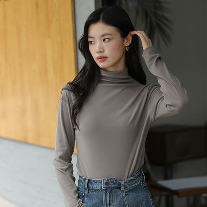 Frau in grauem Rollkragenpullover und blauer Jeans, steht in modernem Innenraum. Mode, Herbstoutfit, lässiger Stil, elegante Kleidung.