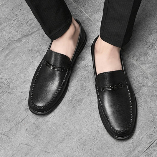 Schwarze Herren-Lederloafer mit Metallschnalle auf grauem Boden, elegante Business-Schuhe, klassische Mode für Herren, stilvoll und bequem.