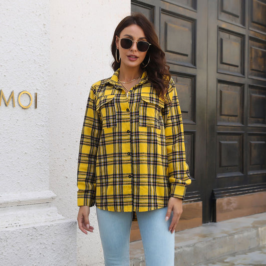 Frau in gelber Karohemdjacke und blauer Jeans vor Holztür, trägt Sonnenbrille und Ohrringe. Modetrend, lässiger Herbstlook, Streetstyle.