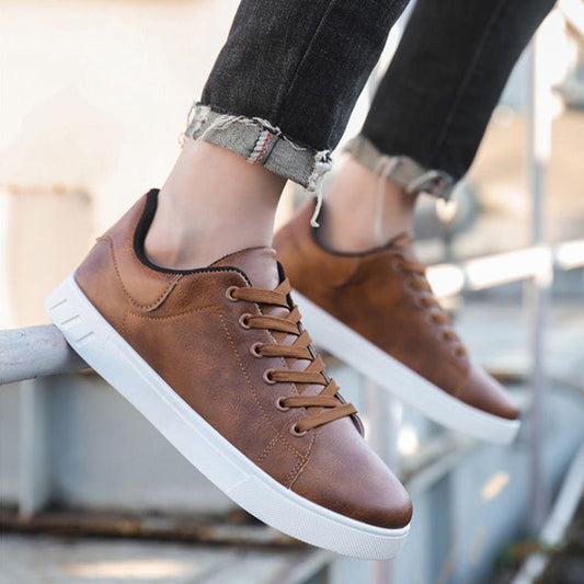 Braune Ledersneaker mit weißer Sohle, getragen von Person in hochgekrempelten Jeans. Modische Freizeitschuhe, ideal für urbanen Stil.