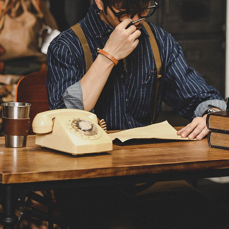 Mann mit Brille liest Dokument am Tisch mit Vintage-Telefon und Kaffeetasse. Retro-Büro, Nostalgie, klassische Büroausstattung.