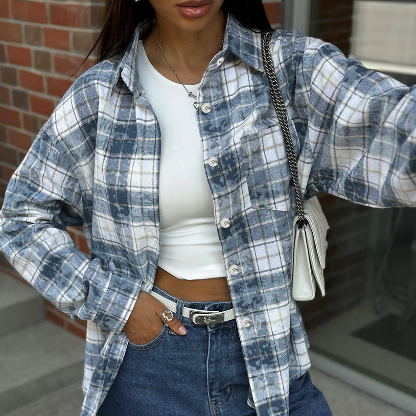 Frau in kariertem Hemd, weißem Crop-Top und blauer Jeans vor Ziegelwand. Modetrend, lässiger Stil, Herbstmode, Damenbekleidung.