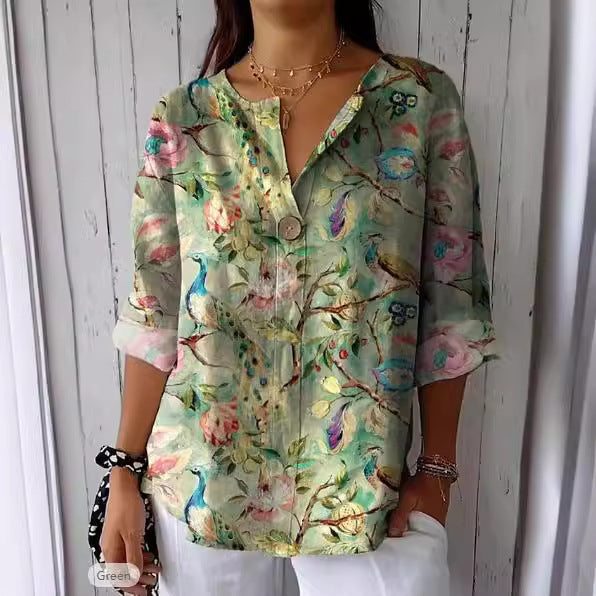 Frau trägt bunte, florale Bluse mit Pfauenmotiv vor Holzwand. Modetrend, Damenmode, Frühlingsoutfit, lässiger Stil, elegantes Design.