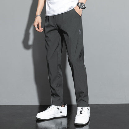 Mann trägt dunkelgraue Chinohose und weiße Sneaker vor grauem Hintergrund. Moderne Herrenmode, lässiger Stil, bequeme Passform.
