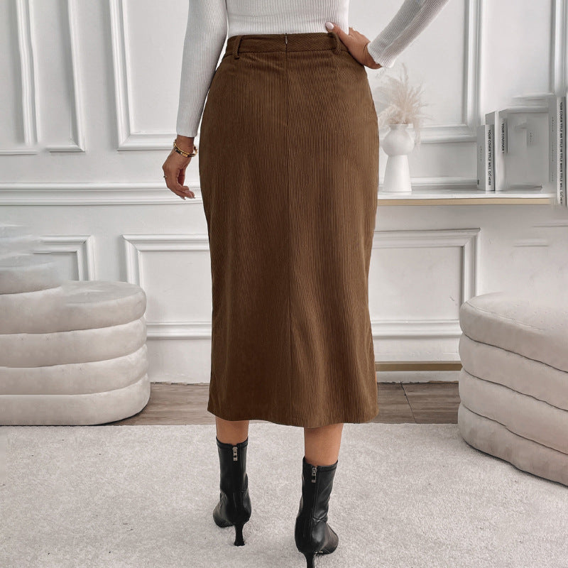 Frau in braunem Cordrock und schwarzen Stiefeletten, steht in elegantem, modernem Wohnzimmer mit weißen Wänden und stilvollen Möbeln.