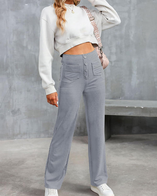 Frau in grauer, hoch taillierter Hose und weißem Crop-Top, posiert vor grauer Wand. Modetrend, lässiger Stil, Streetwear, Damenmode.