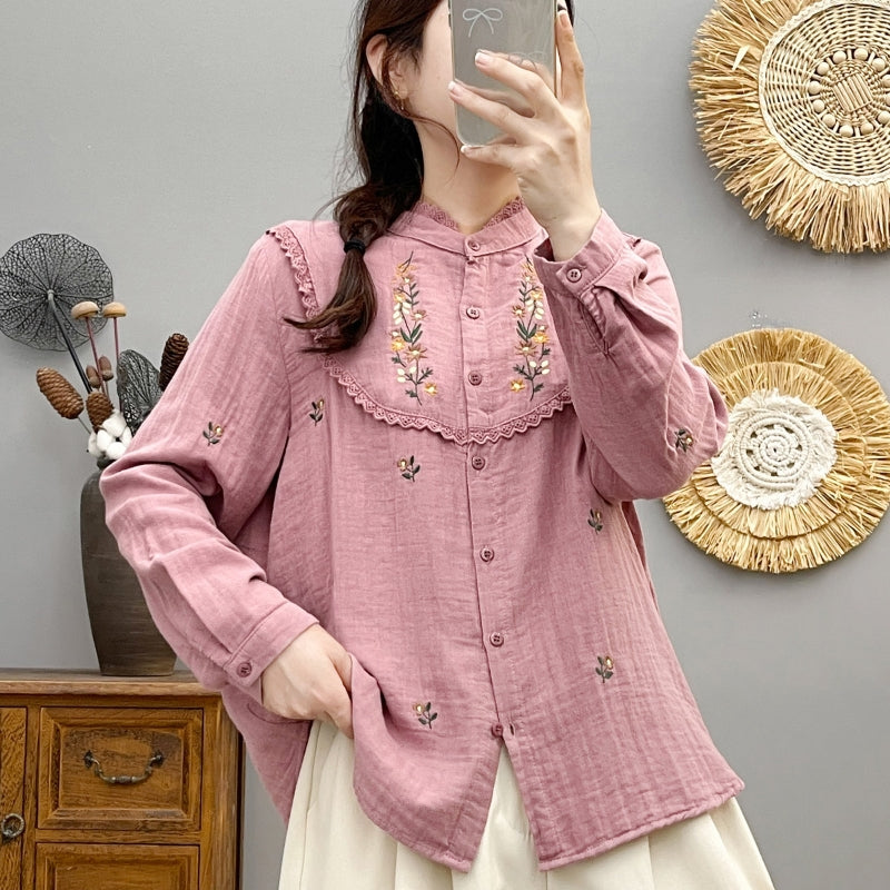Frau in rosa bestickter Bluse macht Selfie, steht vor grauer Wand mit dekorativen Körben. Modetrend, Damenmode, Stickerei, Selfie.