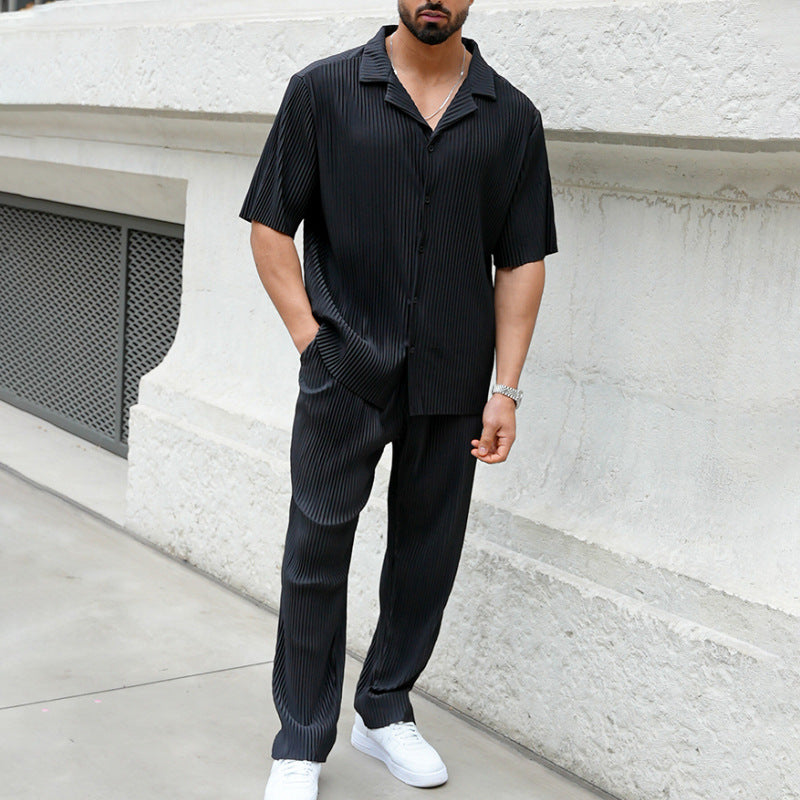 Mann in schwarzem, gestreiftem Hemd und Hose, trägt weiße Sneaker. Stilvolle Herrenmode, lässiger Look, urbane Umgebung.