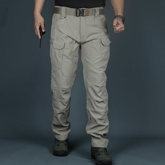 Mann in taktischer Hose, beige, mit Taschen und Gürtel, hält Funkgerät. Outdoor-Kleidung, robust, ideal für Wandern und Abenteuer.