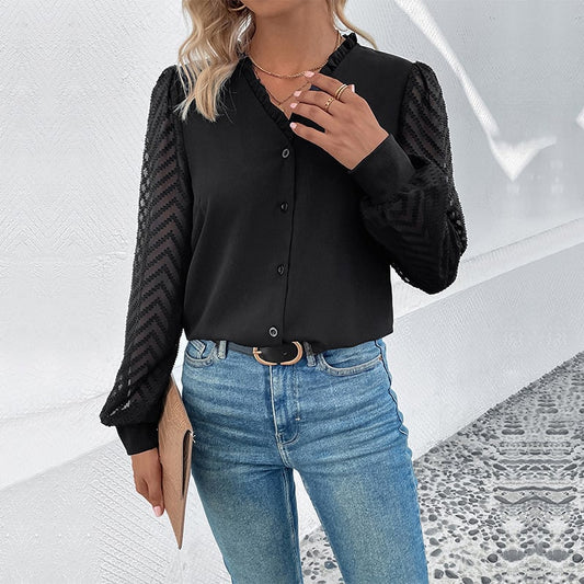 Frau in schwarzer Bluse mit transparenten Ärmeln und blauer Jeans, hält eine beige Clutch. Modetrend, elegante Damenbekleidung, Streetstyle.