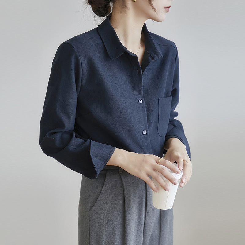 Frau in dunkelblauer Bluse und grauer Hose hält weißen Kaffeebecher. Elegante Business-Kleidung, minimalistischer Stil, Büro-Outfit.