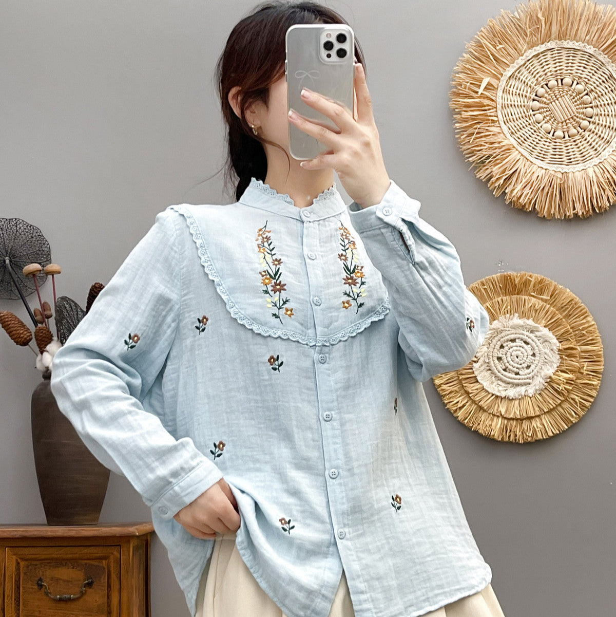 Frau in hellblauer Bluse mit Blumenstickerei macht Selfie. Modetrend, Damenmode, Stickerei, Selfie, Smartphone, Innenraum.