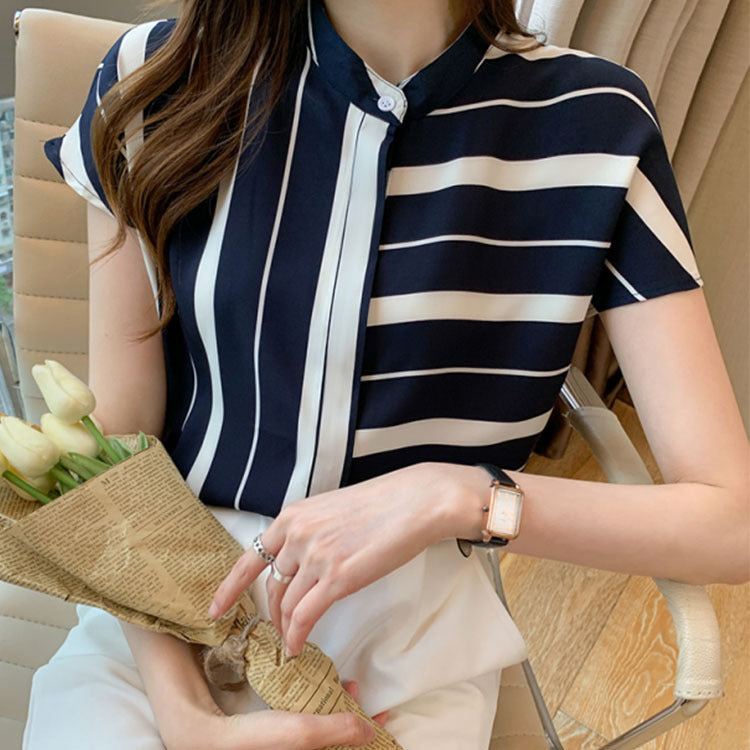 Frau in gestreifter Bluse hält Tulpenstrauß, sitzt auf Bürostuhl. Elegante Mode, Frühlingsblumen, modernes Büro-Outfit.