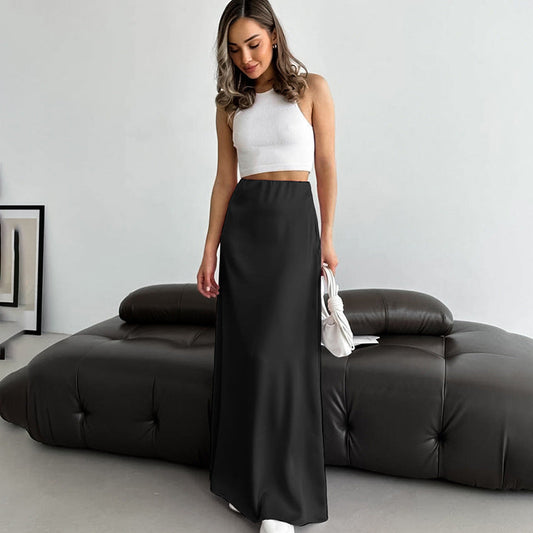 Frau in weißem Crop-Top und schwarzem Maxirock steht vor modernem Sofa. Elegante Mode, minimalistisches Wohnzimmer, stilvolle Inneneinrichtung.