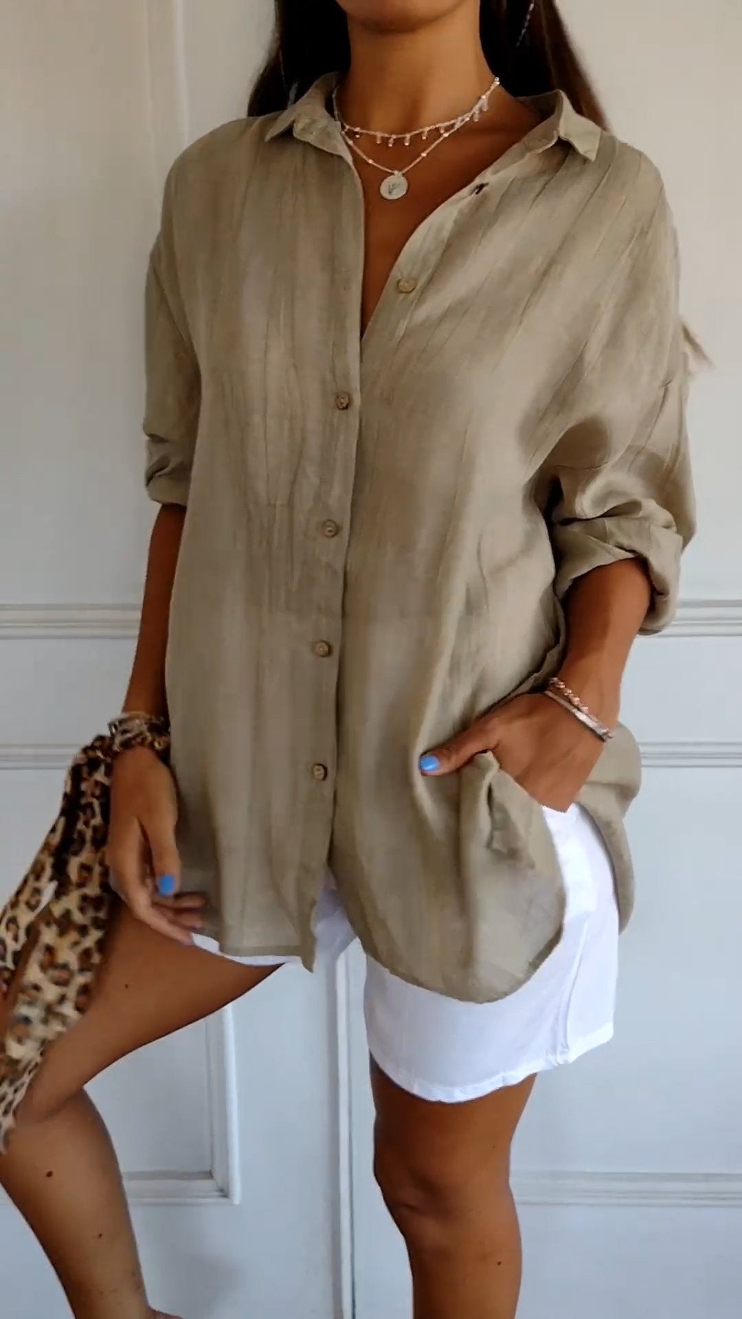 Frau in beigem Leinenhemd und weißen Shorts, hält ein Leopardenmuster-Accessoire. Sommermode, lässiger Stil, trendige Damenbekleidung.