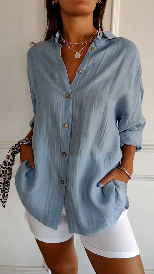 Frau in hellblauer Leinenbluse mit Knöpfen, kombiniert mit weißen Shorts. Modischer Sommerlook, lässig und stilvoll.