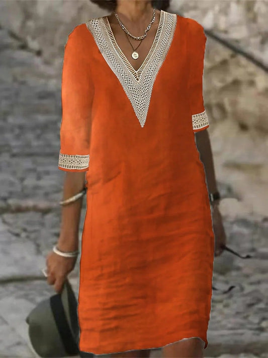 Frau in orangefarbenem Leinenkleid mit V-Ausschnitt und Spitzenbesatz, gehend auf gepflastertem Weg. Sommermode, lässiger Stil, elegantes Design.