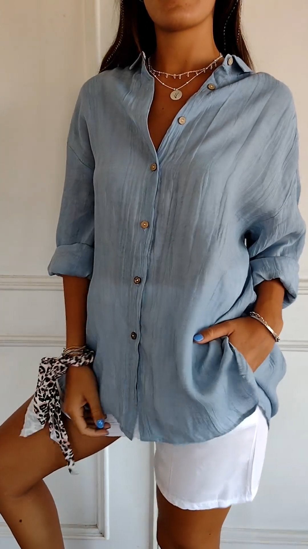 Frau in hellblauer Leinenbluse mit Knöpfen, kombiniert mit weißen Shorts. Sommermode, lässiger Stil, elegante Freizeitkleidung.