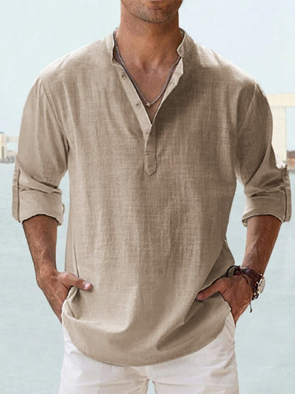 Mann in beigem Leinenhemd mit Stehkragen und hochgekrempelten Ärmeln, lässiger Sommerlook, ideal für Strandmode und Freizeitkleidung.