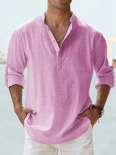 Mann in rosa Leinenhemd mit Stehkragen und Knopfleiste, lässig hochgekrempelte Ärmel, kombiniert mit weißer Hose, modisch und sommerlich.