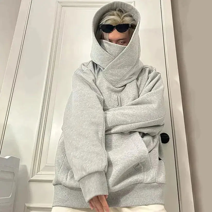 Grauer Oversize-Hoodie, Person mit Sonnenbrille, Kapuze hochgezogen, modischer Streetwear-Look, urbaner Stil, lässige Kleidung.